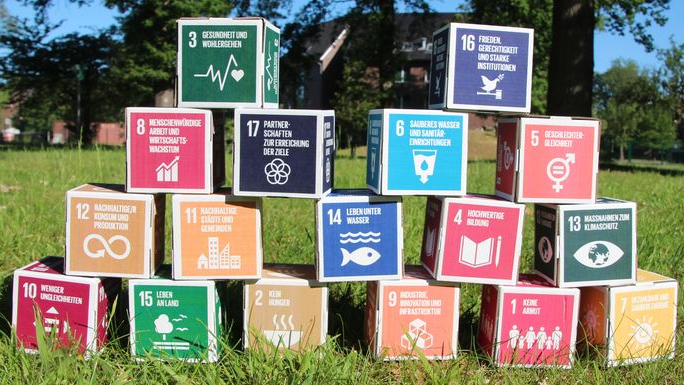 17 Pappwürfel in verschiedenen Farben sind auf einer grünen Wiese übereinander gestapelt