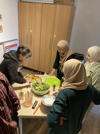 Vier Frauen stehen um einen Tisch auf dem Salat und anderes Essen steht.