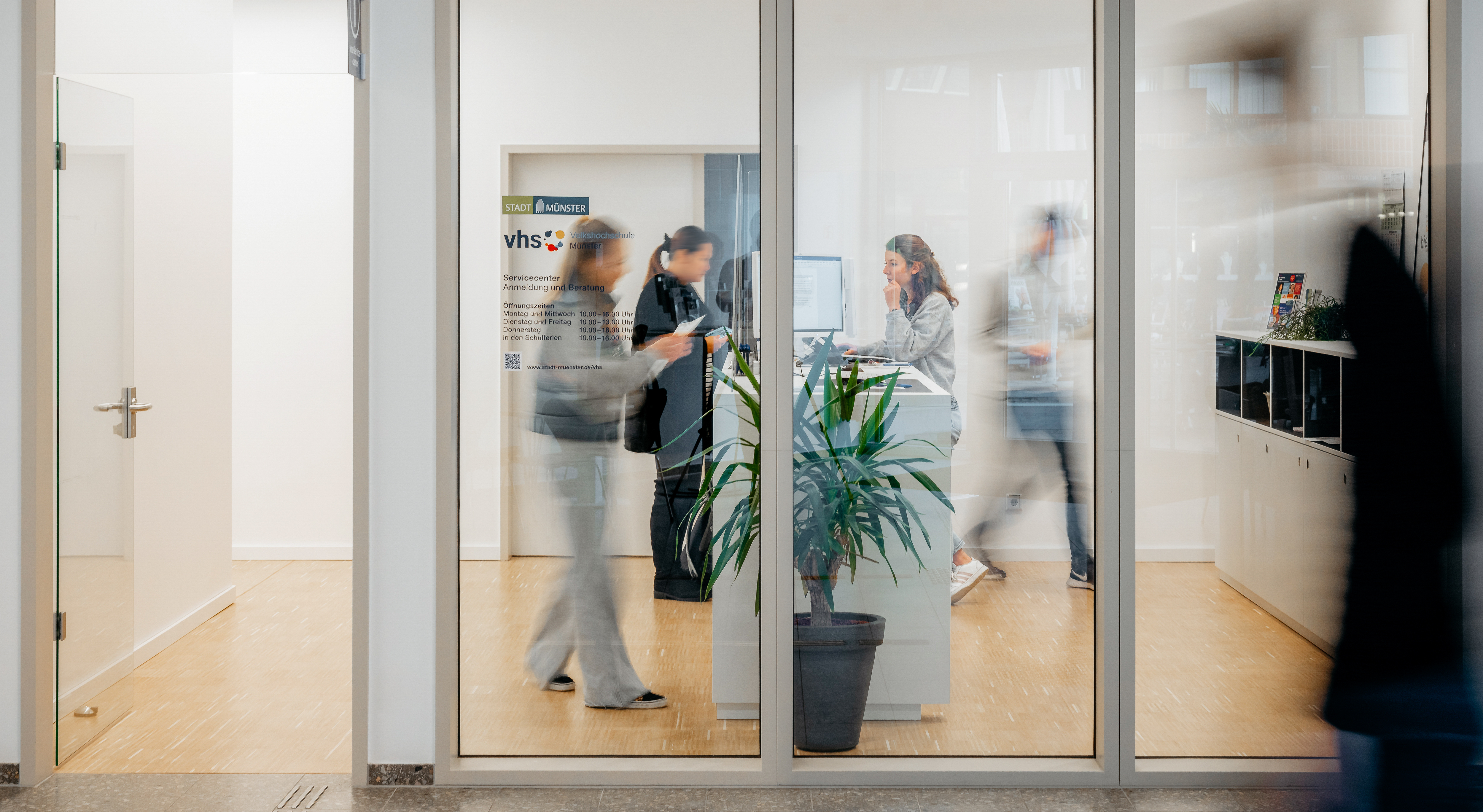 Zwei junge Frauen melden sich an der Theke im Servicecenter der vhs Münster für einen Kurs an.