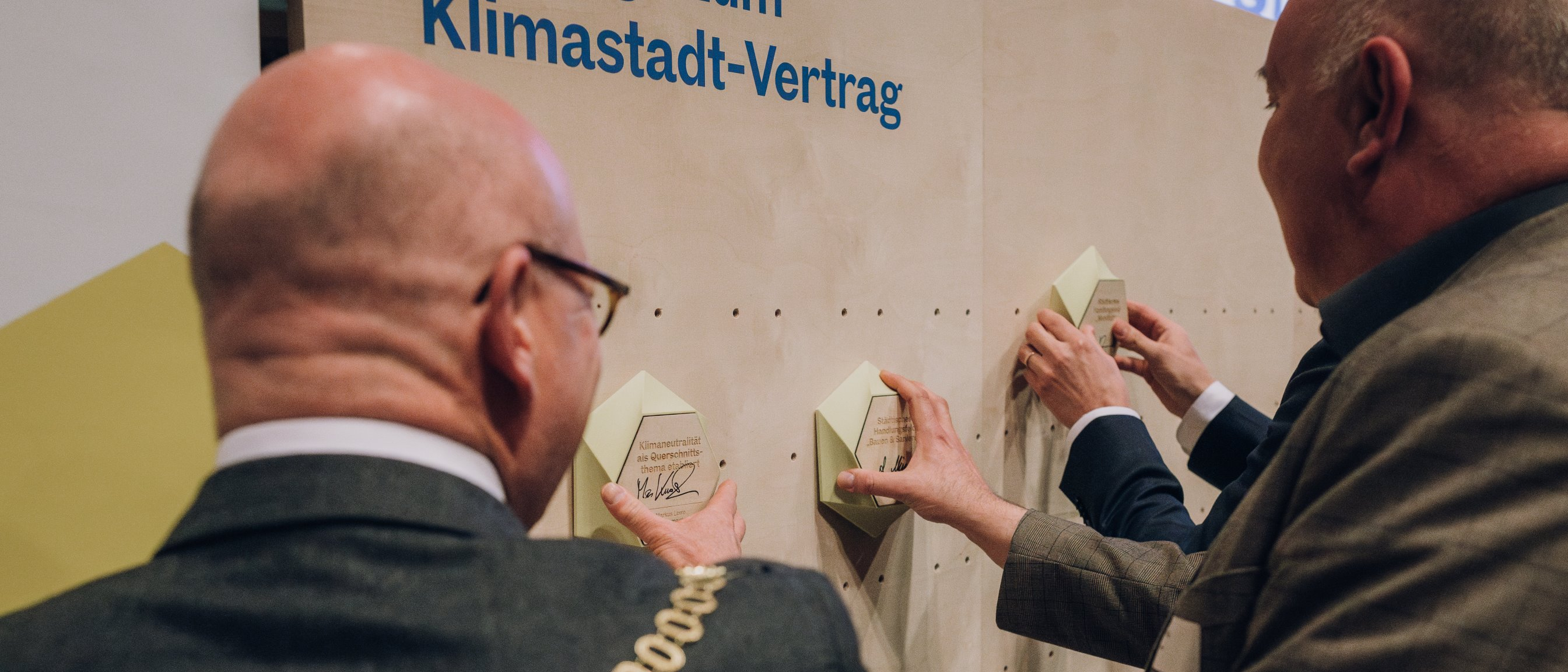 Münsters Oberbürgermeister Markus Lewe befestigt eine Plakette zu einem Beitrag zum Klimastadtvertrag an einer Wand.