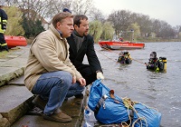 Kommissar Frank Thiel (Axel Prahl) und Rechtsmediziner Prof. Karl-Friedrich Boerne (Jan Josef Liefers) sitzen am Ufer des Aasees und untersuchen einen Müllsack in dem sich eine Leiche befinden soll.
Tatort Mörderspiele, Buch und Regie Stephan Meyer, Erstausstrahlung 2004, Foto: WDR/Michael Böhme.