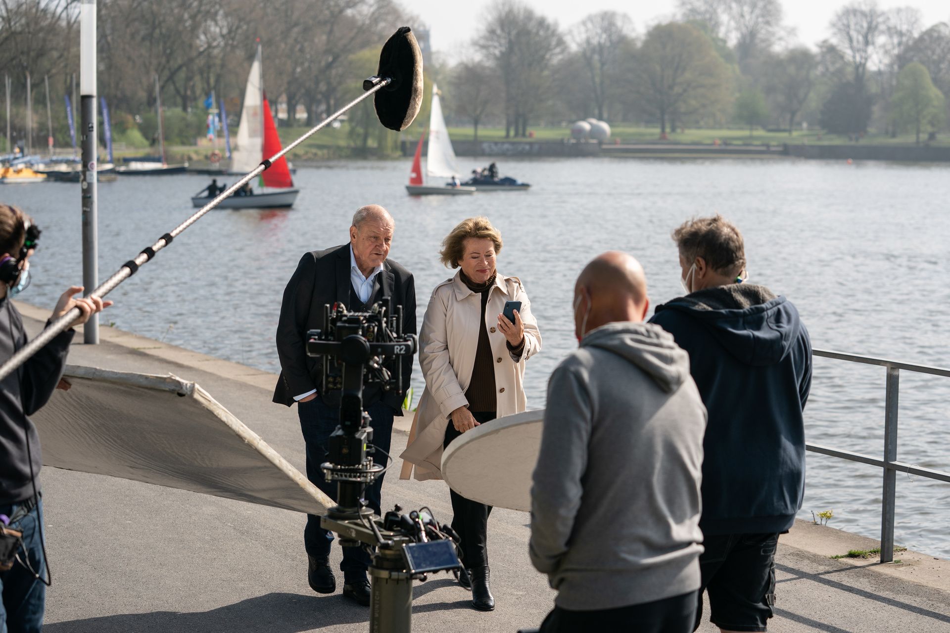 Foto vom Wilsberg-Set am Aasee: Der Wilsbergdarsteller in Aktion im Hintergrund. Im Vordergrund ist das Filmteam zu sehen, welches dem Betrachter den Rücken zukehrt. 