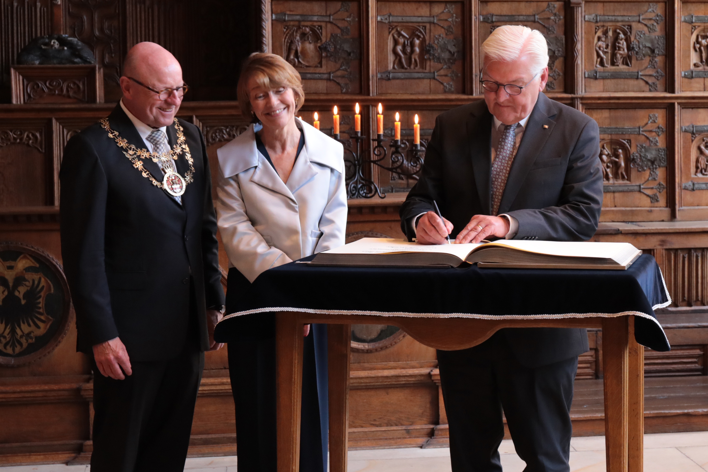 Bundespräsident Frank-Walter Steinmeier trägt sich ins das Goldene Buch der Stadt Münster ein. Daneben stehen dessen Ehefrau Elke Büdenbender und Münsters Oberbürgermeister Markus Lewe.