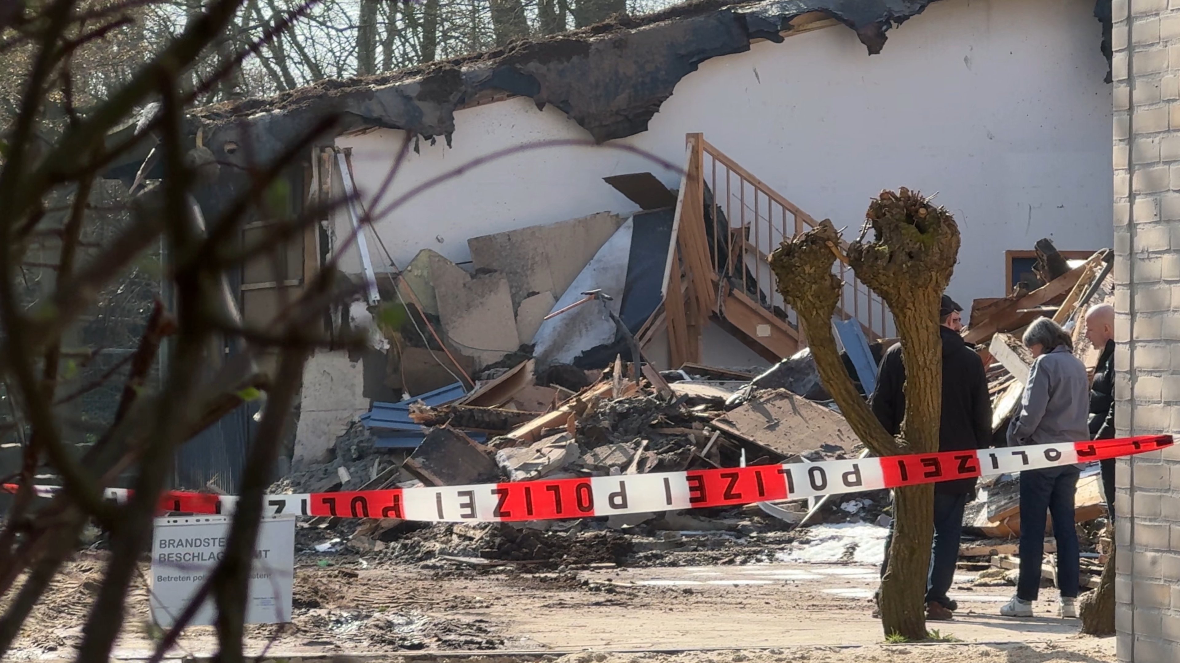 Hinter Absperrband stehen mehrere Personen vor dem abgebrannten Gebäudeteil der Primus-Schule.