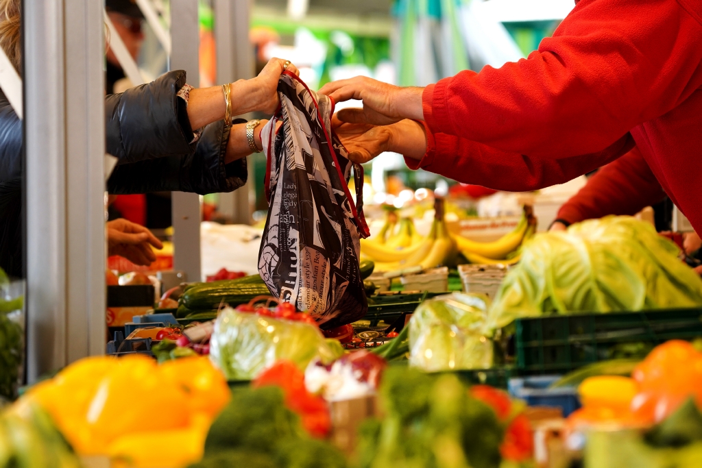 Wochenmarkteinkauf wird über die Gemüseauslage gereicht