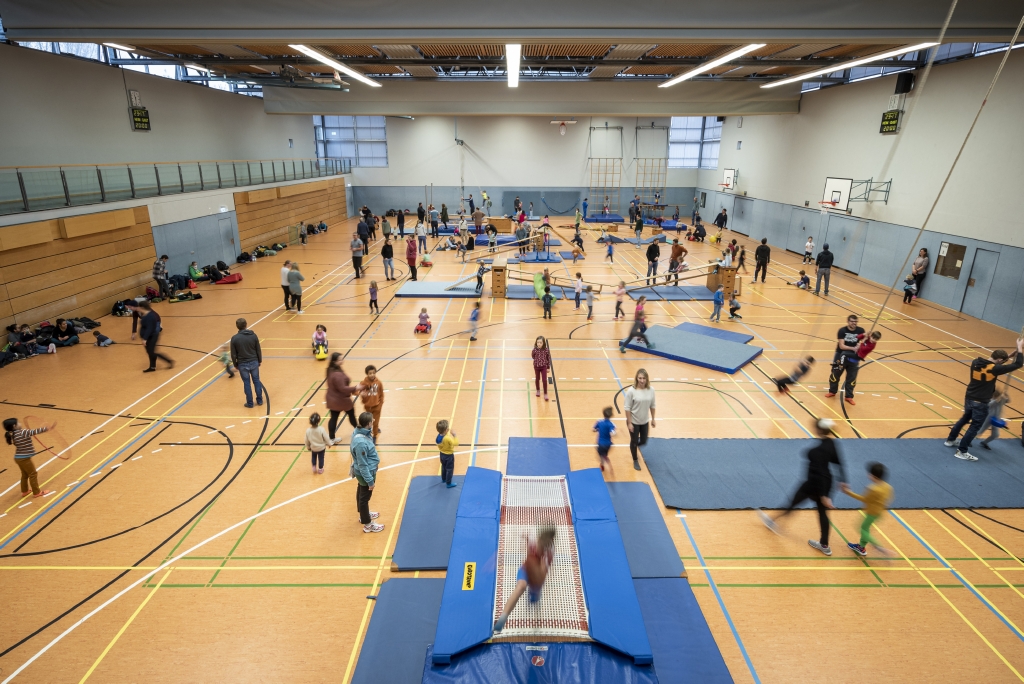 Eine volle Turnhalle mit Eltern und Kindern. 