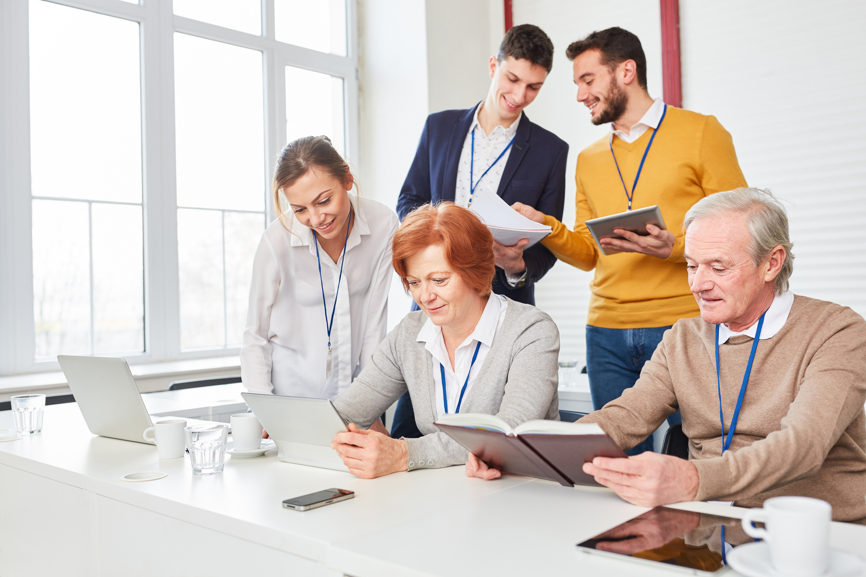 Seniorinnen und Senioren sitzen vor einem PC und befinden sich vor einer Dozentengruppe in einer Lernsituation