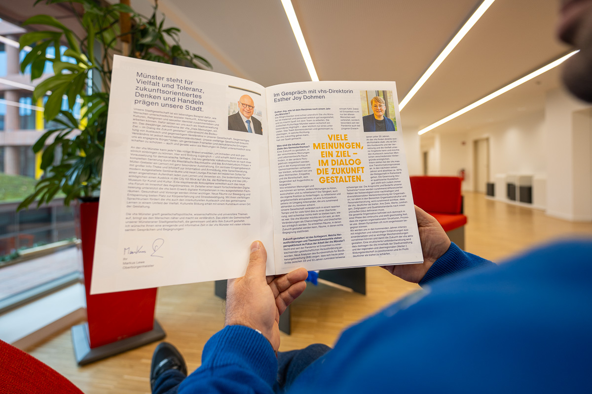 Ein Mann sitzt im Aufenthaltsbereich der vhs auf einem Sofa, hält das neue Programm-Magazin in der Hand und liest darin.