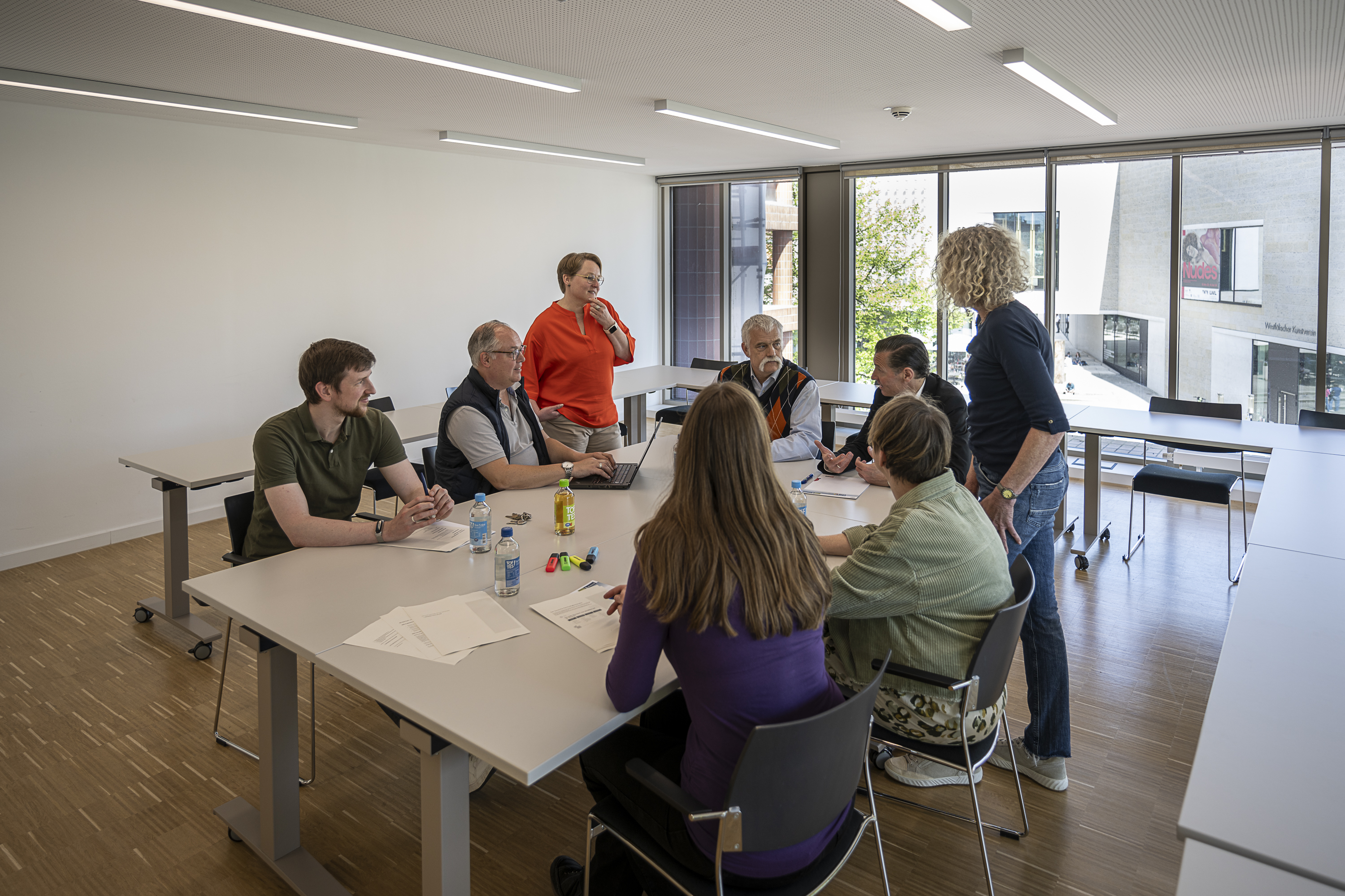 Mitarbeitende der vhs Münster beraten und disktutieren gemeinsam am Konferenztisch im Büro.