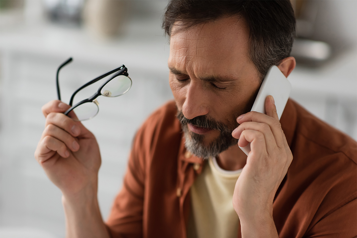 Mann telefoniert mit dem Handy und hält eine Brille in der rechten Hand