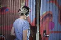 Eine Besucherin in Rückenansicht trägt einen Kopfhörer. Sie steht vor einer Tür und ist kurz davor den Parcours ‚Gesichertes Gelände‘ zu betreten.