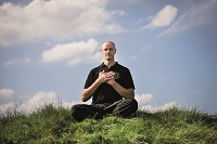 Der Qi Gong - Leher Volker Nowak-von der Way sitzt im Schneidersitz auf einem Hügel.