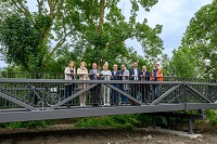 9 Personen stehen auf der neuen Brücke, im Hintergrund Baumbewuchs.