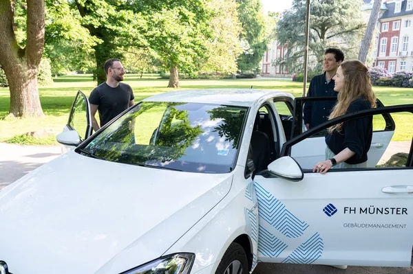 Drei Personen stehen um ein Auto herum mit Aufschrift der FH Münster.