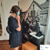 Eine junge Frau steht in der Ausstellung der Villa vor einem historischen Foto einer Deportation in Bielefeld.