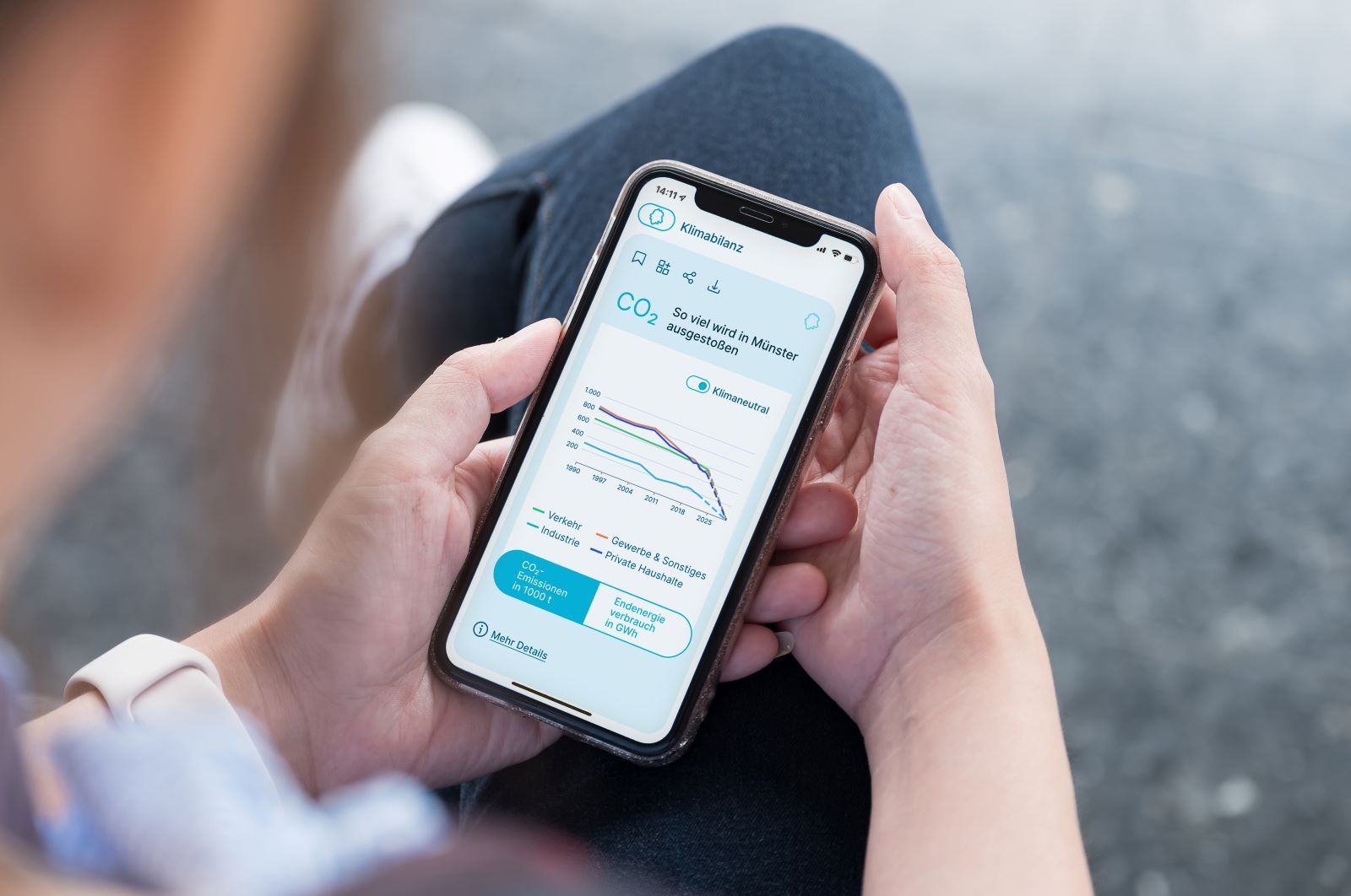 Eine Person hält ein Smartphone in der Hand. Auf dem Bildschirm ist die Website Klimadashboard Münster geöffnet.
